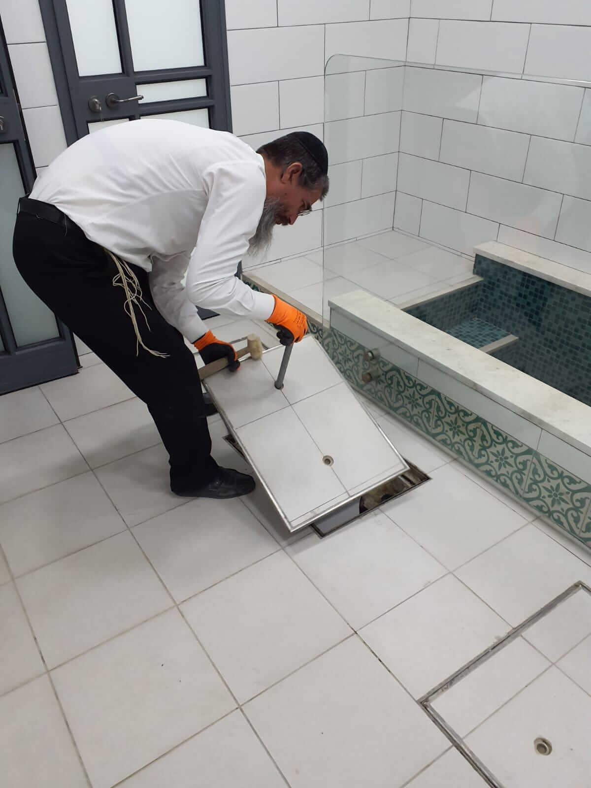 רב כשרות מרים את מכסה פתח הביקורת ברצפת המקווה